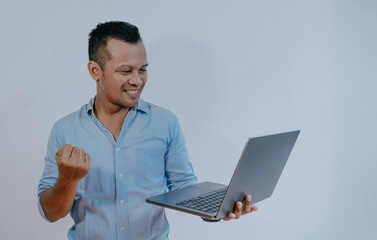 Indonesian businessman holding laptop computer and gesturing yes, Celebrating big luck browsing internet standing on white background. Successful online business, Technology Concept.