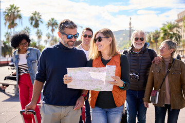 Couple of middle-aged walking and looking and holding a travel map with a group diverse tourist...