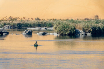Fisherman in a rowboat on the Nile river at sunet, scenic landscape with rocks in the water and...