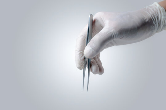 Close up Doctor's hand with Latex gloves taking the 
stainless tweezers to help the patience people on white gray background.