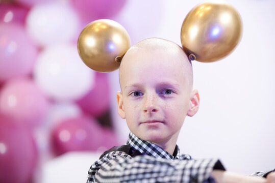 A bald boy of 12 years old with inflatable balls on his head, like the ears of a mouse.