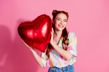 Portrait of cheerful girlish woman with foxy hairstyle wear print shirt holding heart shape bubble isolated on pink color background