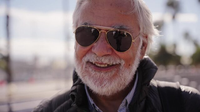 Portrait of Caucasian mature man tourist with beard and white hair happy and smiling looking at camera enjoying their holidays wearing sunglasses outdoor on a winter sunny day. Copy space