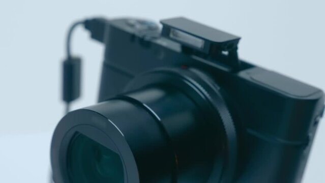 A portable black camera with a zoom lens on a tripod takes a picture with flash on a white background. Closeup. Macro. Shot in motion