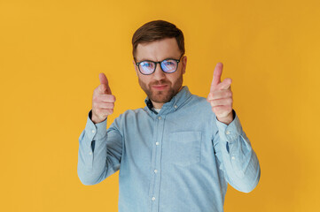 Pointing fingers to the front. Attractive man in blue shirt is against yellow background