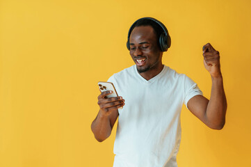 Listening to the music, holding smartphone. Black man is in the studio against yellow background