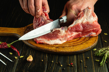 A butcher cuts meat with a knife. Cutting pork ribs by a chef's hands on a kitchen table before preparing a fatty dish.