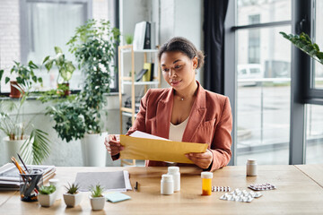 focused african american nutritionist reviewing envelope near supplements on her working desk