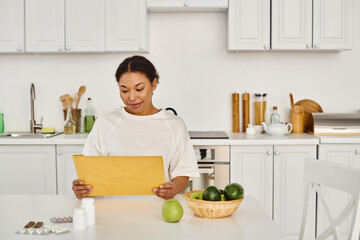 brunette african american woman looking at envelope with dietary plan near supplements and fruits