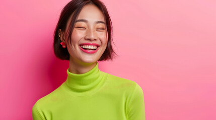 Exuberant Joy: Asian Woman Laughing with Eye-Catching Green Top on Pink Background - obrazy, fototapety, plakaty