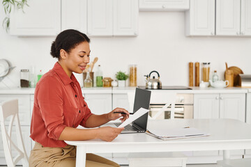 cheerful african american nutritionist reviewing documents near laptop for online consultation