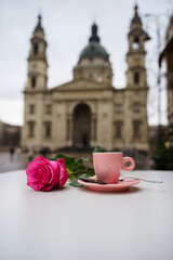 A pink rose and a coffee cup on a table in front of basilica
