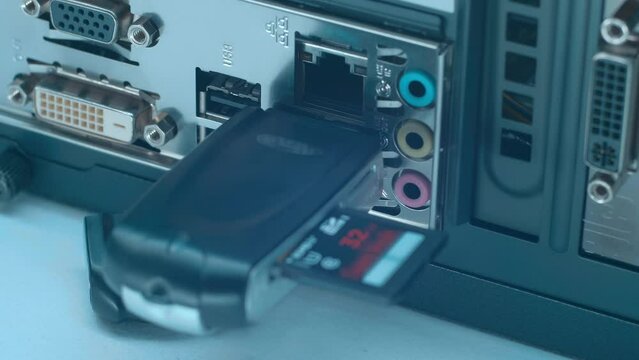 A man's hand inserts and removes a SD card reader into the USB port on the back panel of the computer. Closeup. Macro