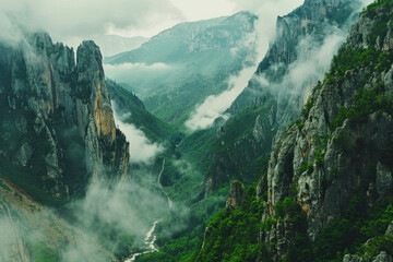Cinematic shot of the view from above, looking down at an epic mountain range with clouds rolling over and mist hanging in between mountains, green grass on cliffs - obrazy, fototapety, plakaty