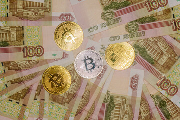 Gold and silver bitcoins on Russian banknotes with a face value of one hundred rubles.