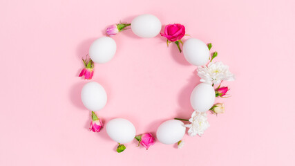 White eggs arranged in a circle are decorated with buds of natural flowers. Pink background. Easter holiday.