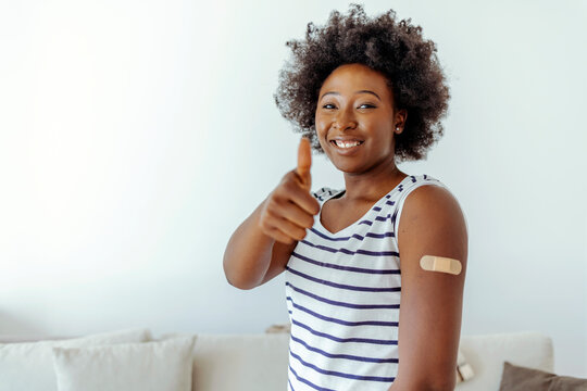 Young african american woman showing thumb up and her arm with band aid after coronavirus Covid-19 vaccine injection. Covid vaccination concept.