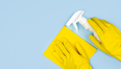 Cleaning concept. Woman's hands in yellow gloves, rag and cleaning spray on a blue background. Close-up. Top view. Copy space.