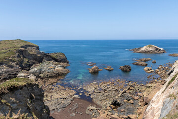 A scenic coastline with rocky formations, blue waters, and distant mountains under a clear sky,...