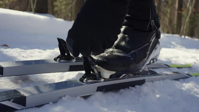 A male skier fastens ski boots into cross-country ski fasteners in close-up. Close-Up of Cross-Country Skiing Equipment on Snow. Training of an athlete in the fresh air on a ski run. 