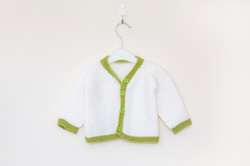 Knitted green and white daisy button baby cardigan on hanger