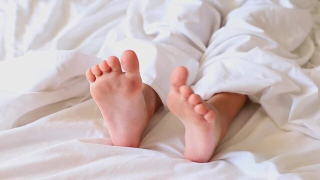 Little girl's feet stick out from under a white blanket at the morning. 
