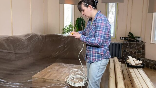A woman engages in home improvement, planning renovation on backdrop of construction materials indoors. Reconstruction, DIY concept. Handywoman preparing an electrical wire, stripping the insulation