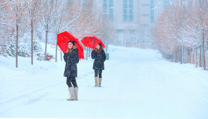 Beautiful girl in black coat with red umbrella walking down the road while snowfall