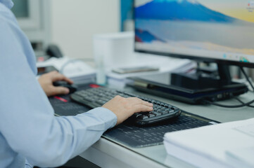 Businessperson or is typing on a computer keyboard. The person is wearing a blue shirt and is using a black keyboard in office
