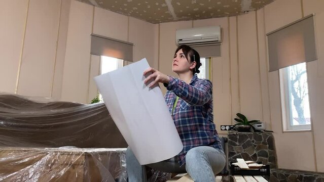 A beautiful young woman engages in home improvement, planning preparing for renovation on backdrop of construction materials indoors. Reconstruction, DIY concept. Handywoman considers remodeling plan