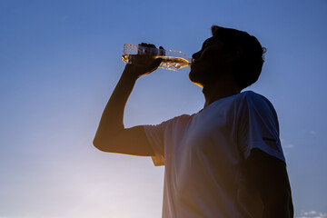 Silhouette of young man runner with a bottle of water freshness after training outdoor workout.	