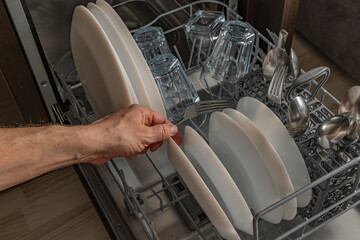 A man stacking dishes in the dishwasher helps in the kitchen to save water