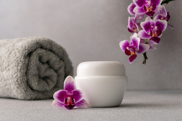 Obraz na płótnie Canvas White cosmetic cream jar, product mockup on gray background with orchid flower and towel
