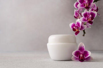 White cosmetic cream jar, product mockup on gray background with orchid flower