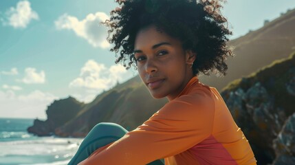 afro woman with sporting clothes is sitting near the ocean in a natural environment