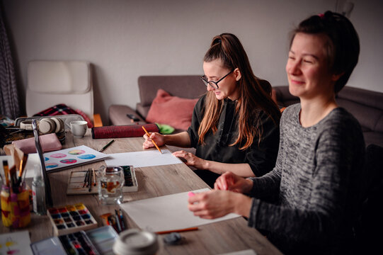 Two women engage in an artistic collaboration, they drawing together in a cozy creative space