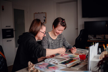 Fototapeta premium Two artists share a moment of creation, painting with watercolors in a home setting, showcasing teamwork and artistic expression