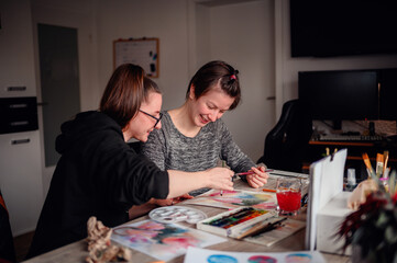 Fototapeta premium Two artists share a moment of creation, painting with watercolors in a home setting, showcasing teamwork and artistic expression