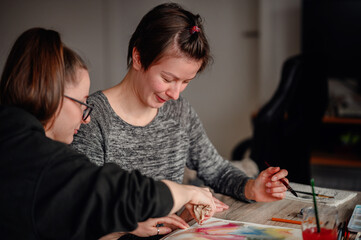 Fototapeta premium Two friends share laughter and joy while engaged in watercolor painting, illustrating the pleasure of artistic hobbies.