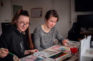 Fototapeta premium Two artists share a moment of creation, painting with watercolors in a home setting, showcasing teamwork and artistic expression