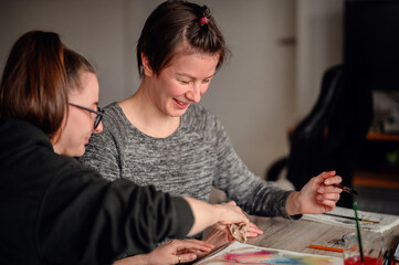 Two friends share laughter and joy while engaged in watercolor painting, illustrating the pleasure of artistic hobbies.