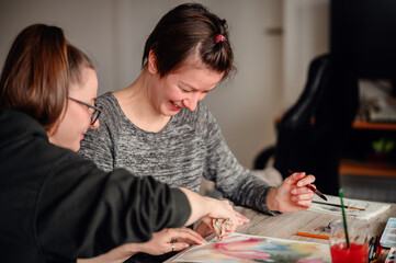 Fototapeta premium Two friends share laughter and joy while engaged in watercolor painting, illustrating the pleasure of artistic hobbies.