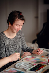 An artist smiles gently while immersed in the flow of watercolor painting, surrounded by art...