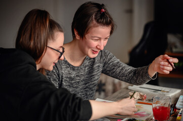 Two friends share laughter and joy while engaged in watercolor painting, illustrating the pleasure...