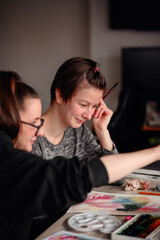 Fototapeta premium Two friends share laughter and joy while engaged in watercolor painting, illustrating the pleasure of artistic hobbies.