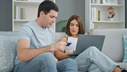Fototapeta premium Beautiful couple shopping with laptop and credit card sitting on sofa at home