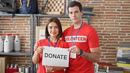 Man and woman volunteers standing together holding paper with donate message at charity center