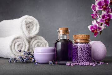 Fototapeta na wymiar Spa wellness set with lavender flowers, orchid, essential oil bottles, cream jar, and purple granules for aromatherapy