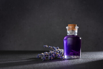 Small glass bottle with purple liquid of lavender syrup and with lavender flowers on a dark...