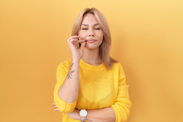 Young caucasian woman wearing yellow sweater mouth and lips shut as zip with fingers. secret and...